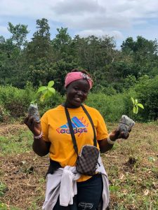 Smiling woman wearing a pink headband standing among young tree seedlings and forest, Sierra Leone